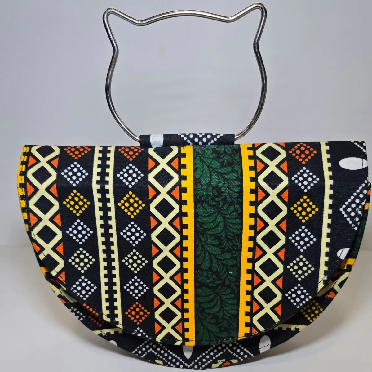 Vibrant Ankara-patterned clutch bag with a semi-circular shape and a unique metal handle shaped like cat ears, displayed on a plain white background.