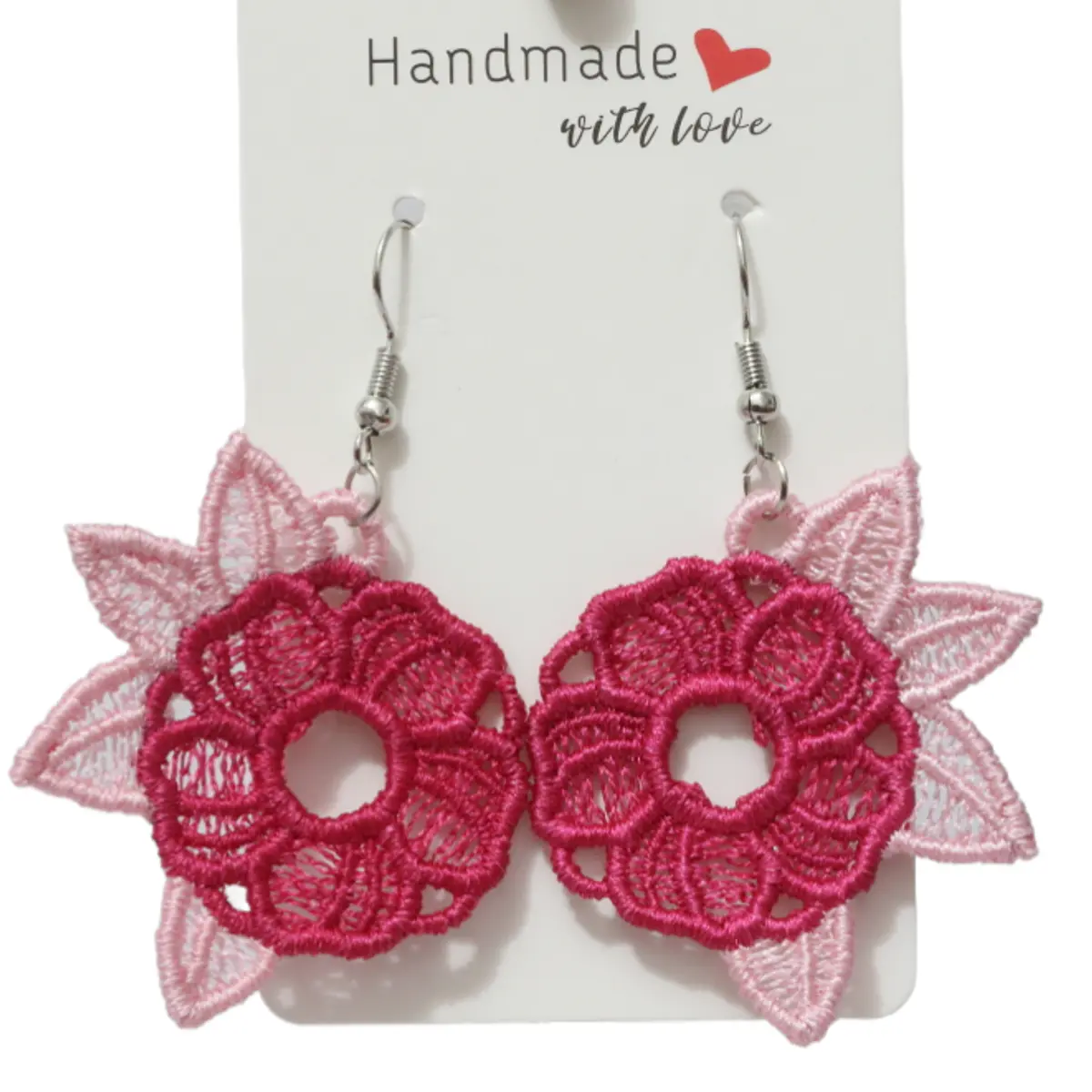 A pair of handmade lace floral dangle earrings displayed on a white card tag reading 'Handmade with love.' Each earring features a deep fuchsia pink embroidered flower center with an open lace design, framed by soft blush pink embroidered leaf petals, hanging from silver fish hook wires. Color: Fuchsia Pink and Blush Pink