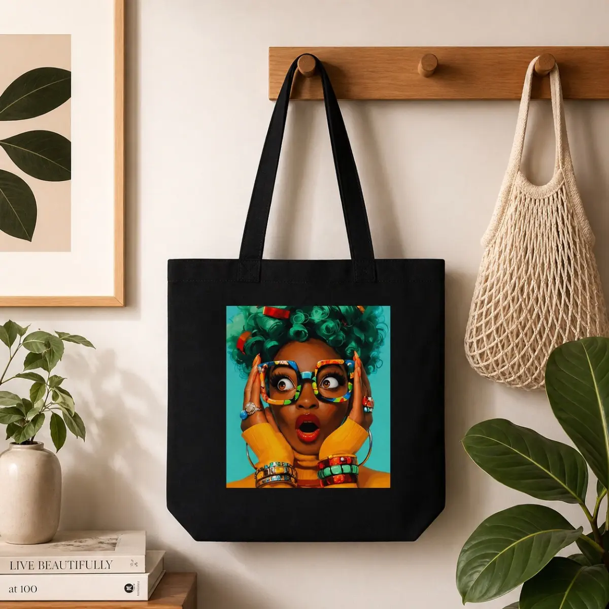 A black canvas tote bag hung on a wooden wall hook, featuring a vibrant square print of a stylized Black woman with teal curly hair, colorful accessories, and an expressive surprised expression on a turquoise background. The bold, hand-designed African-inspired graphic art print is centered on the bag's front panel, showcasing artisan-quality craftsmanship with rich, vivid colors. The sturdy canvas construction and matching black shoulder straps make it both a functional and wearable piece of art. Color: Black, Teal, Yellow, Multicolor