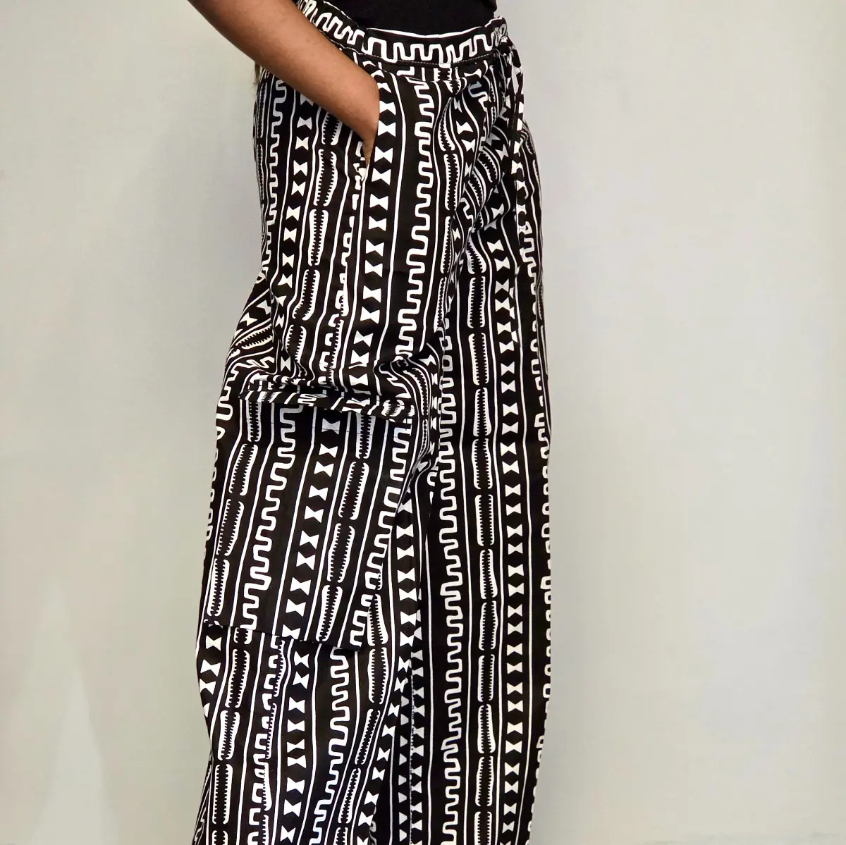 Side profile view of handmade African print palazzo pants in a bold black and white geometric Ankara pattern. The wide-leg silhouette and deep side pocket are clearly visible, with the model's hand resting inside the pocket. Color: Black and White